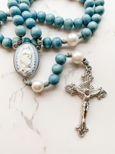 "This handcrafted, beautiful, and unique Catholic rosary is made with 8mm dyed blue beads and 10mm natural pearl beads. The beads are strung and knotted on micro cord (the slimmest type of paracord!) for durability. The cameo rosary center depicts our Lady of Guadalupe. The crucifix is 2 inches in length and was made in Italy. This rosary is about 14 inches in length and is lightweight and easy to carry with you so you can \"pray without ceasing.\" Each rosary from Refuge Rosaries is carefully p Cheap Handmade Spiritual Rosary, Affordable Blue Rosary Bracelet As Gift, Rosary Case, Pray The Rosary, Rosary Beads Catholic, Praying The Rosary, Pray Without Ceasing, Catholic Rosary, Rosary Bracelet