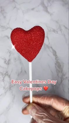 a hand holding a heart shaped lollipop with the words easy valentine's day cake pops on it