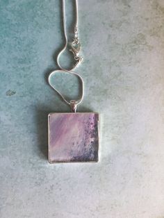 This is a portion of an acrylic pour that has been set in a silver plated bezel and coated with resin. The pour is different thicknesses so part of the silver bezel shows through for texture and added interest. This is such a pretty necklace in soft shades of lilac and little glimpses of a darker blue and is just what you need to compliment your spring wardrobe. This pendant is perfect for any female in your life, any occasion, but would be perfect for Mother's Day. Every care has been taken to capture the colours of this one off piece of jewellery, but bear in mind all screens and monitors are different. It is not recommended that you wear this jewellery in water. Artsy Purple Jewelry For Gifts, Modern Resin Jewelry For Gifts, Modern Resin Jewelry Gift, Rectangular Silver Jewelry Gift For Her, Artsy Silver Round Pendant Jewelry, Artsy Nickel-free Silver Jewelry, Artsy Silver Jewelry With Large Pendant, Nickel-free Silver Resin Jewelry, Rectangular Resin Jewelry Gift