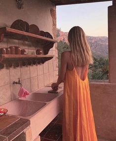 a woman in a yellow dress is standing by a sink and looking out the window