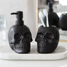 two skull shaped soap dispensers with toothbrushes in them on a marble plate