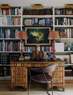 a desk with two lamps on top of it next to a book shelf filled with books