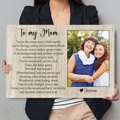 a woman holding up a wooden plaque with the words to my mom in front of her