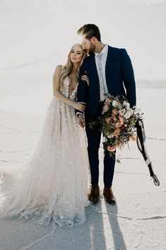 a bride and groom standing in the snow with their arms around each other holding bouquets