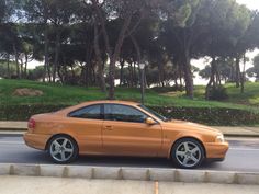 an orange car is parked on the side of the road in front of some trees