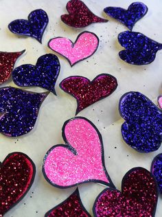 some hearts are laying on a table with purple and pink glitters in the shape of hearts