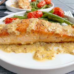 a white plate topped with salmon and green beans next to tomatoes on top of a table