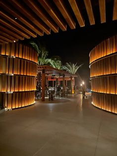 an outdoor dining area at night with palm trees and lights on the wall behind it