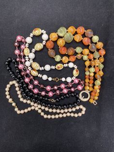 "This collection of beaded chokers will add 80s style throughout the year. With classic faux pearls, springtime flowers, bright pinks, autumnal orange, and dark black these necklaces are useful with a variety of styles and occasions. Included in the collection: --faux pearl 17\" necklace with ball clasp; has gold tone tag that says \"marvella\". --pink and purple 18\" necklace with smaller beads in between larger beads; has springring clasp. --white floral 16.5\" necklace with painted red and white flowers and springring clasp; some paint has chipped. --double strand 15.25\" orange, green, and brown necklace with toggle hook clasp; clasp has heavy patina. --black 17\" necklace with springring clasp and white cord visible between beads; two beads are fused together. See photos. These are us Red And White Flowers, Brown Necklace, 80s Style, Hook Clasp, Choker Necklaces, The 1980s, Beaded Necklaces, Beaded Choker, Vintage Wear