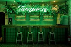 a bar with green neon lights and stools in front of the bar is filled with plants