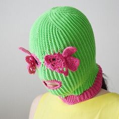 a woman wearing a green knitted hat with pink flowers on the top and bottom