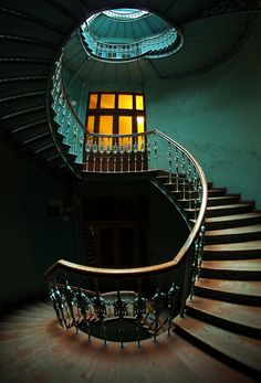 a spiral staircase in an old building with glass railings and lights on the windows