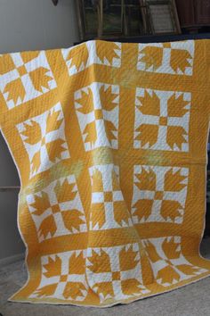 a yellow and white quilt on the floor next to a table with a chair in front of it