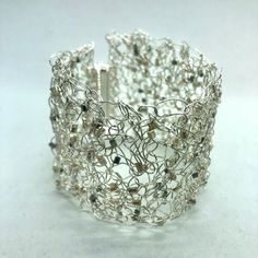 a silver wire bracelet with lots of beads on the outside and inside, sitting on a white surface