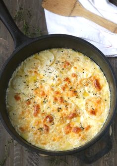 a skillet filled with cheese and sauce on top of a wooden table next to a white towel