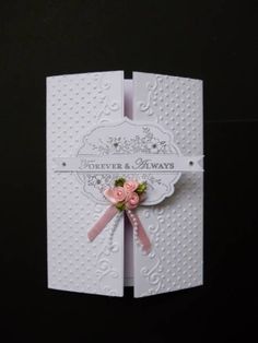 a white card with pink ribbon and flowers on the front, sitting against a black background