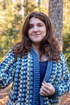 a woman standing in the woods wearing a blue and white crocheted cardigan