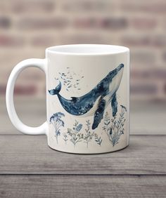 a coffee mug with a whale painted on the front and bottom, sitting on a wooden table