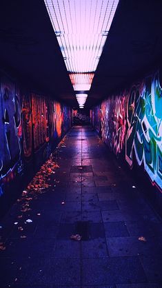 a long hallway with graffiti on the walls and ceiling above it is lit by a bright light