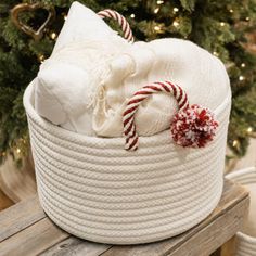 a white basket filled with candy canes on top of a wooden bench next to a christmas tree