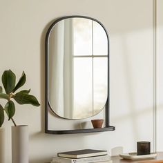 a mirror sitting on top of a wooden table next to a vase and bookcase