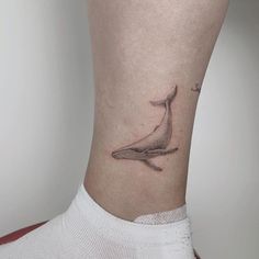 a small whale tattoo on the side of a woman's leg, with an anchor