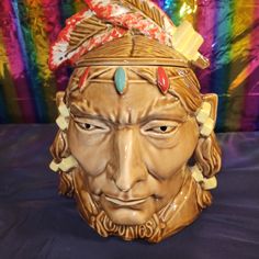 a ceramic mask with feathers on it's head is shown in front of a colorful background