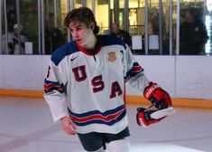 a young man in an ice hockey uniform is holding his gloves and looking at the camera