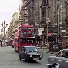 a red double decker bus driving down a street next to tall buildings with scaffolding