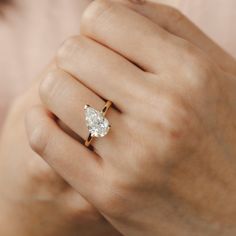 a woman's hand holding a ring with a pear shaped diamond on it,