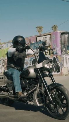 a man riding on the back of a motorcycle down a street next to graffiti covered walls