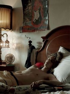 a shirtless man laying on top of a bed next to a lamp and clock