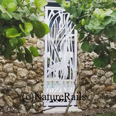 a white metal gate sitting in front of a stone wall next to a green leafy tree