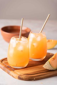 two glasses filled with watermelon juice sitting on a cutting board next to slices of melon