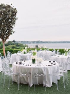 the tables are set with white linens and clear chairs for an outdoor wedding reception