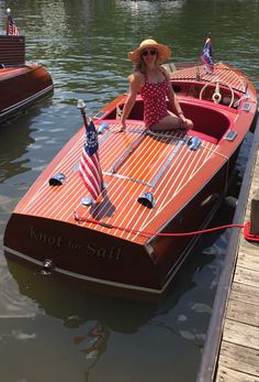 a woman sitting on top of a wooden boat in the water with an american flag