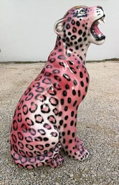 a pink and black cheetah statue sitting on gravel with its mouth wide open