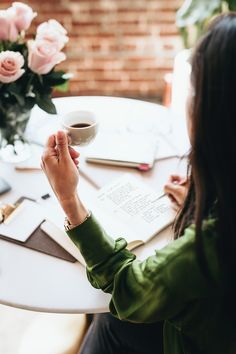 a woman sitting at a table with a cup of coffee and notebooks on it