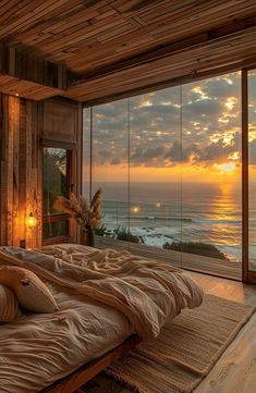 a bedroom with a large window overlooking the ocean and sunset in the sky, along with an unmade bed