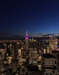 an aerial view of the city at night with skyscrapers lit up in purple and blue