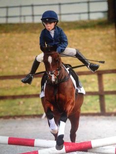 a young person riding on the back of a brown and white horse over an obstacle