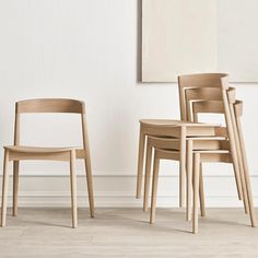 three wooden chairs sitting next to each other in front of a painting on the wall