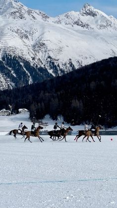 a group of people riding on the backs of horses across snow covered ground with mountains in the background