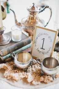 a table topped with books and cups filled with liquid next to a teapot, candle and other items