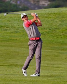 a man swinging a golf club on top of a green field