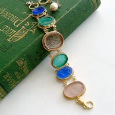 A stunning collection of Venetian glass cameo/intaglios in lapis blue, emerald green and blush pink, have been married together to create this classic bracelet. Each of the gorgeous intaglios/cameos sits in bezeled mountings accented with a twisted border made of gold vermeil. This neoclassical design is simultaneously understated and dynamic with it’s simple classic designs and coloring. This jaw-dropping bracelet with roots in the Byzantine era, will quickly become a favorite due to its classi Elegant Handmade Glass Bracelets, Elegant Glass Jewelry With Cabochon, Elegant Oval Glass Jewelry, Elegant Glass Bracelet Jewelry, Elegant Blue Glass Bracelets, Elegant Blue Glass Bracelet, Neoclassical Design, Blue Emerald, Vintage Designer Jewelry