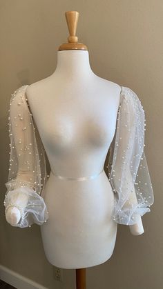 a white mannequin with sheer sleeves and pearls