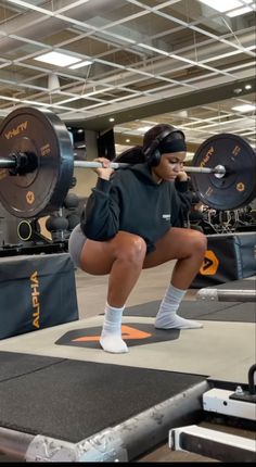 a woman squats on the floor in front of a barbell weight machine while wearing headphones