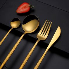 four forks, two spoons and one strawberry on a black surface with gold trim