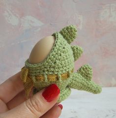 a crocheted green toy with an egg in it's mouth is held up to the camera